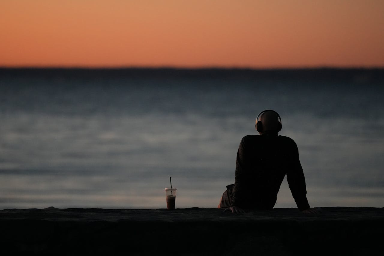 Person with headphones enjoys a peaceful sunrise by the water at Cove Island Park, Stamford.