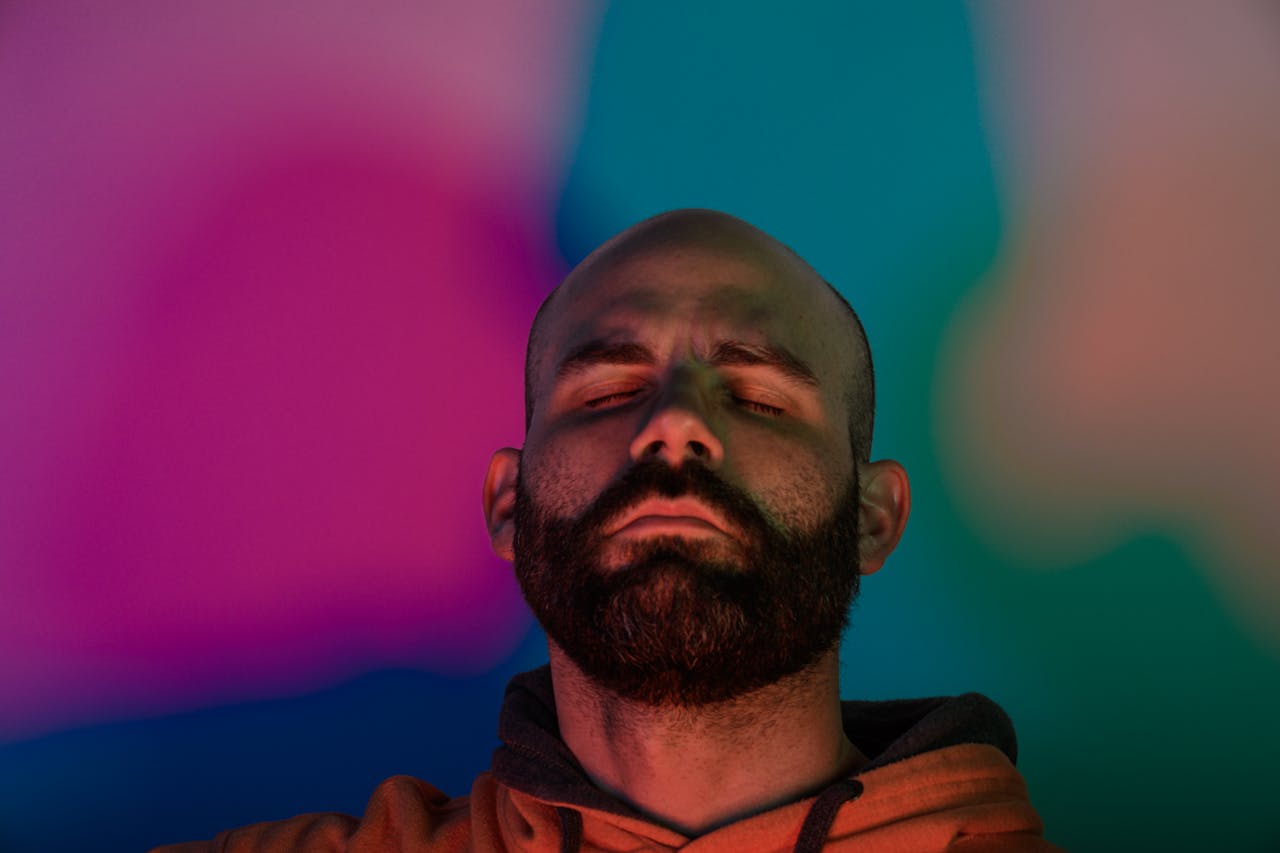 Artistic portrait of a bearded man with eyes closed, surrounded by vibrant, colorful light patterns.