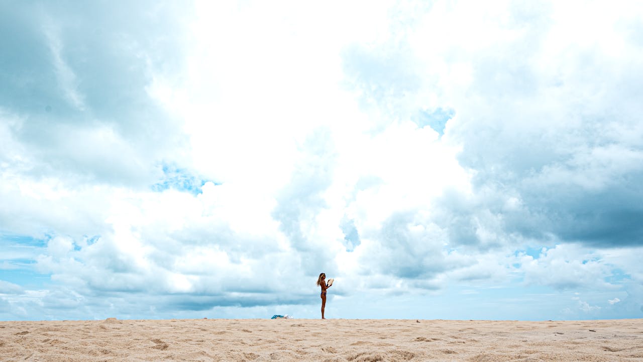 Woman practicing yoga alone on a sandy beach under a vast, cloudy sky in Natal, Brazil.